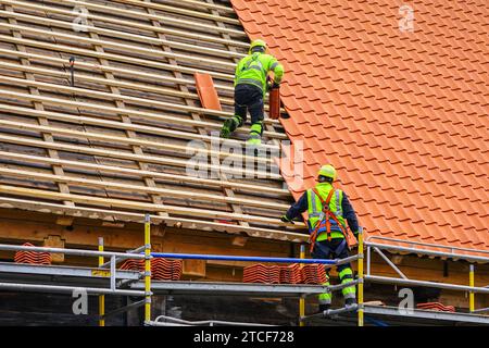 Two roofers in protective workwear installing new clay tiles, new clay tiles layer covering Stock Photo