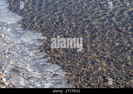 Ice forming at lake's edge, with clear water and stones Stock Photo