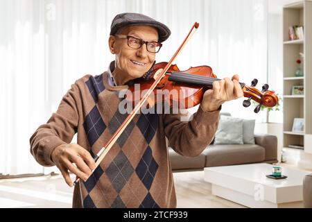 Happy pensioner playing a violin at home in a living room Stock Photo