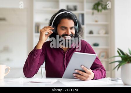 Handsome Indian Man Wearing Wireless Headphones Using Digital Tablet At Home Stock Photo