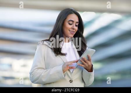 Latin entrepreneur woman smiling using smartphone app outside office building Stock Photo