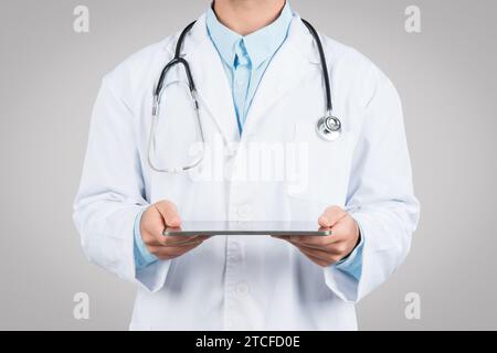 Medicine and technologies. Unrecognizable male doctor using digital tablet, standing on grey studio background Stock Photo