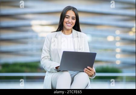 Happy Arabic businesswoman working on laptop sitting in city Stock Photo