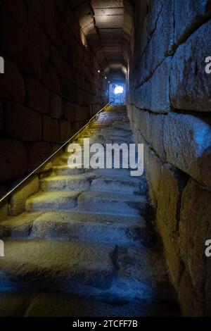 Ancient stone staircase used to access water leading to a bright exit in a dimly lit tunnel, symbolizing hope and direction. Stock Photo