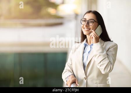 Happy inspired young caucasian businesswoman in suit talking on mobile phone on light office space Stock Photo