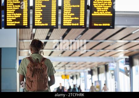 Rear View Of Man Wearing Backpack Looking At Train Departure Board In Railway Station Stock Photo