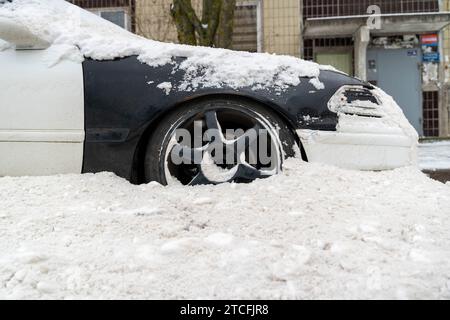 A snow-covered passenger car is parked on a street, appearing buried in snow after a snow removal. The vehicle is surrounded by a thick layer of snow, Stock Photo