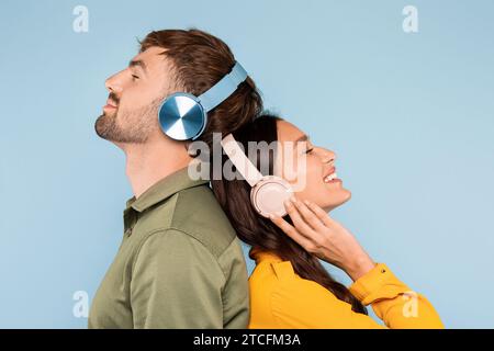 Joyful man and woman in headphones enjoying music, standing back-to-back Stock Photo