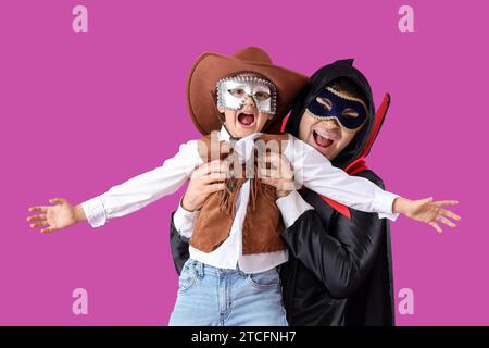 Happy father and son in costumes and carnival masks on purple background Stock Photo