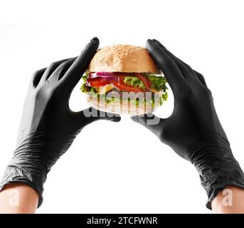 Hands in black gloves hold a juicy, appetizing beef burger on a white background. Hamburger in hands isolated. Banner, fast food advertising. Stock Photo