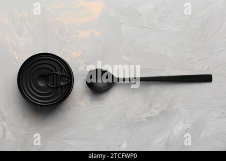 Black matte round closed tin can and black spoon on gray texture background top view, tinned food, canned food, preserves. Stock Photo