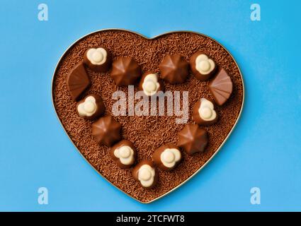 Heart-shaped box with chocolates and chocolate chips on a blue background, top view. Postcard, template for Valentine's Day. Stock Photo