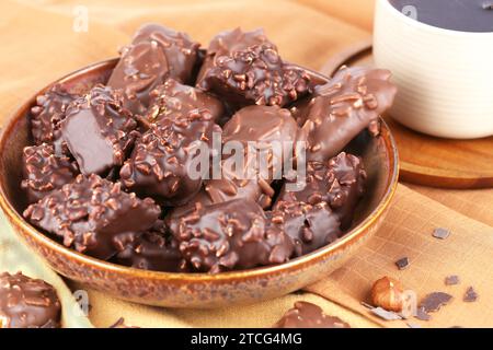 Chocolate with hazelnuts in ceramic bowl and cup of tea on the brown fabric background. Stock Photo