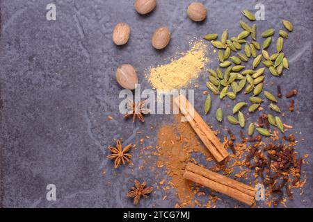 Flat lay of spices on a dark background. Top to bottom Nutmeg, White pepper, Cardamom, Cloves, Star Anise, Cinnamon. Stock Photo