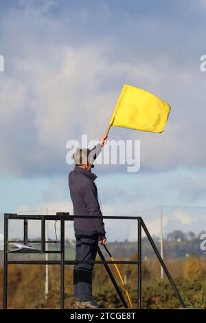 Starter and starting flag UK National Hunt race.Man with yellow flag starting horse-race under orders at Down Royal Racecourse, Lisburn, Northern Ireland. Stock Photo