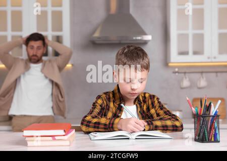 Father getting annoyed while son doing his homework in kitchen, selective focus. Dyslexia problem Stock Photo