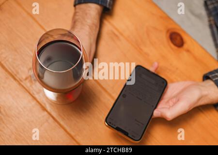 Close-up shot of a man with a glass of wine and holding a phone to track amount of alcohol or to rate a wine in an app. Stock Photo