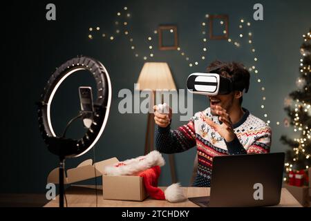 Arab male blogger unboxing parcel with VR Glasses at Christmas Eve at camera, young man using smartphone on tripod recording video for tech blog at Stock Photo