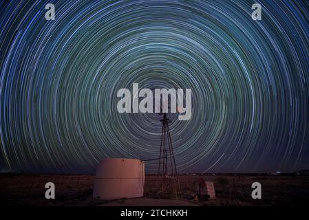 Star trails caused by the Earth's rotation captured above a wind-powered water pump on a WA cattle station. Stock Photo
