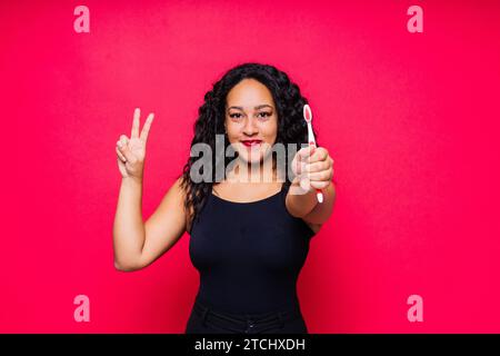 Happy African American woman brushes teeth. Dental hygiene concept. Isolated on red background. Stock Photo