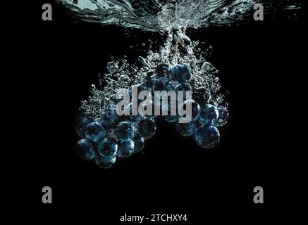 Bunch of red grapes splashing into clear water isolated against black background. Food splash photography. Healthy fruits theme Stock Photo