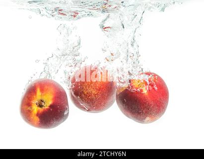 Three peaches falling into water with splash Stock Photo