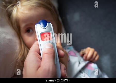 Mother takes temperature for her child with infrared thermometer at home, low-grade fever Mother hand holding digital infrared thermometer Stock Photo