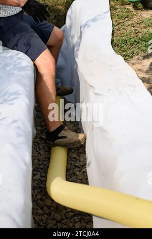 A worker stands in a drainage trench with white geotextile. Feet of the craftsman on the granite rubble close up. Stock Photo