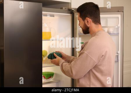 Man putting bowl covered with beeswax food wrap into refrigerator indoors Stock Photo