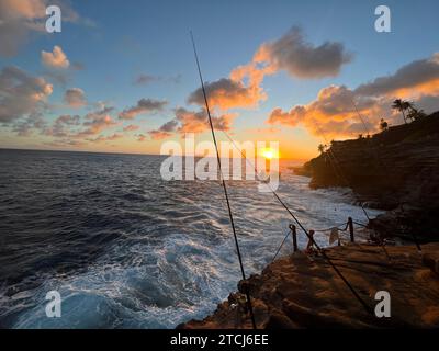 A man stands on a rocky coastline, fishing in the evening Stock Photo