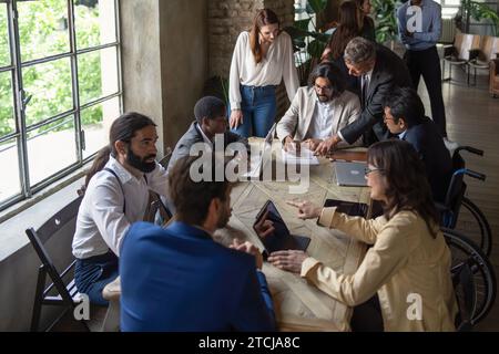 Diverse team members engage in a collaborative meeting in a bright, modern office space, emphasizing inclusivity and teamwork. Stock Photo