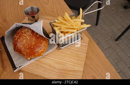 Burger in wrapping paper and french fries in a metal mesh basket on a table at open air snack bar Stock Photo