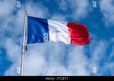 The French flag in the wind in front of a blue sky with veil clouds and a beautiful light. The flag has the color blue white and red Stock Photo