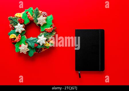 Christmas wreath of gingerbread and black notebook on red background Stock Photo