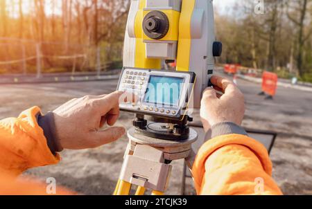 Site engineer operating his instrument during roadworks. Builder using total positioning station tachymeter on construction site for new road setting Stock Photo