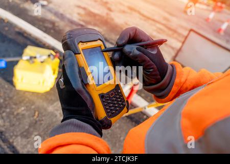 Site engineer operating his touch screen controller instrument during roadworks. Builder using touch screen controller to control total positioning st Stock Photo