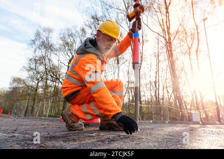 Surveyor operating his touch screen controller instrument during surveying roadworks and marking point on asphalt  using chalk Stock Photo