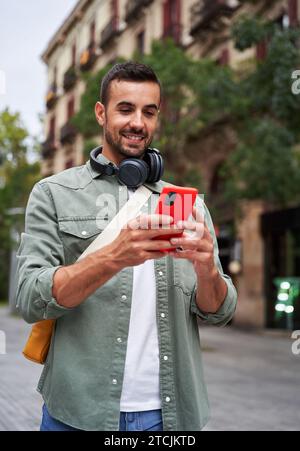 Cool smiling young caucasian man holding mobile standing on the street in the city. Stock Photo