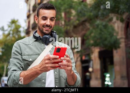 Cheerful young caucasian man holding mobile standing on the street in the city. Stock Photo