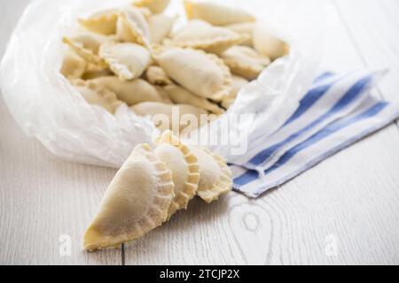 Raw dumplings with filling inside, Ukrainian cuisine. Raw dumplings for freezing in a bag on a light wooden table. Home kitchen. Stock Photo