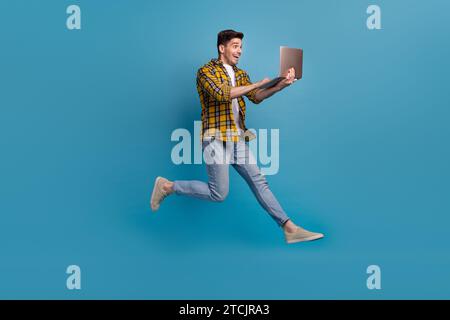 Full body length photo addicted programmer loves doing his job in deadline running jumping with computer isolated on blue color background Stock Photo