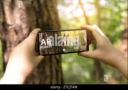 Hand of a woman experiencing an augmented reality (AR) application using a smartphone in the forest Stock Photo
