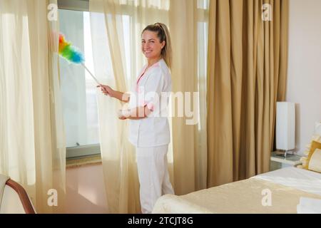 Image of beautiful hotel maid cleaning room with a duster. Stock Photo