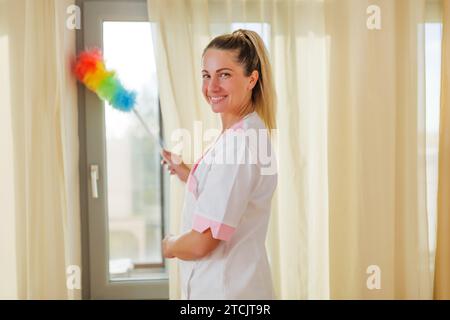 Image of beautiful hotel maid cleaning room with a duster. Stock Photo