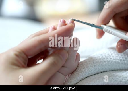 The mother's hand holds a nail clipper, and the other hand holds the  newborn's hand, Mom