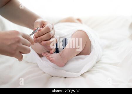 Mother's hands cutting newborn baby's toenails with scissors Stock Photo