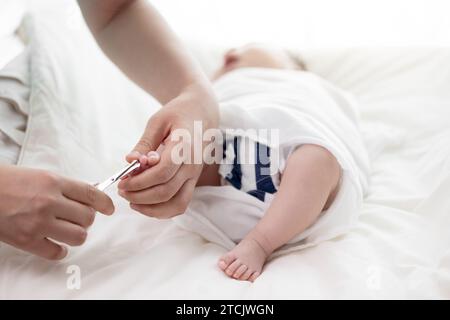 Mother's hands cutting newborn baby's toenails with scissors Stock Photo