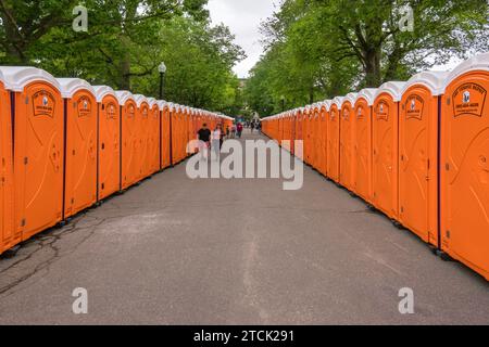 Boston, MA US-June 10, 2023: Two rows of orange portable toilets at a large outdoor event. Stock Photo