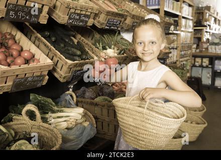 Girl choosing vegetables in vegetable shop. on the signboard inscriptions in Catalan Stock Photo