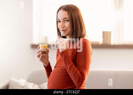 Young pregnant lady enjoys tasty snack eating sweet dessert indoors Stock Photo